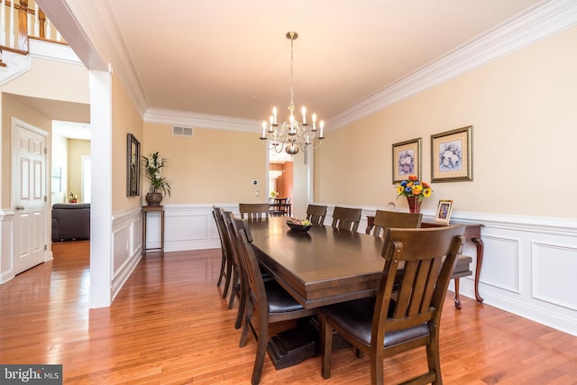 dining area with light wood-type flooring, visible vents, a notable chandelier, crown molding, and a decorative wall