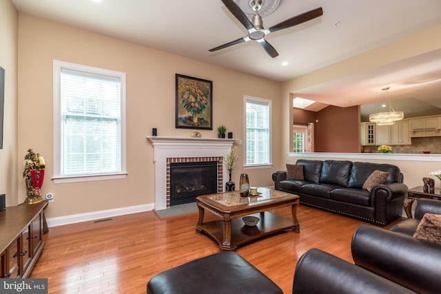 living area with visible vents, a brick fireplace, baseboards, lofted ceiling, and light wood-style floors