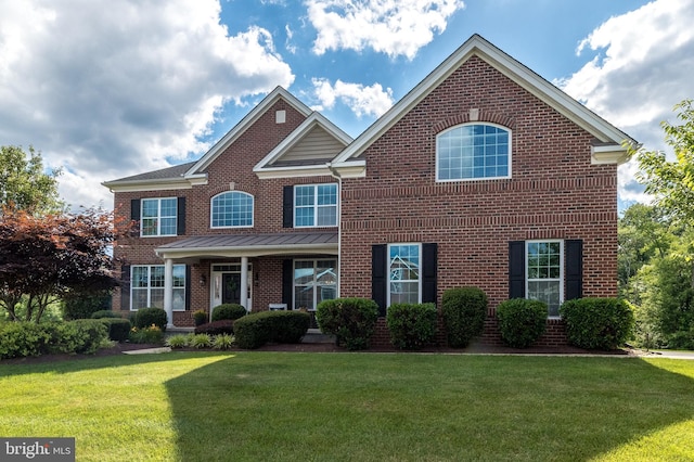 view of front facade featuring a standing seam roof, a front lawn, brick siding, and metal roof