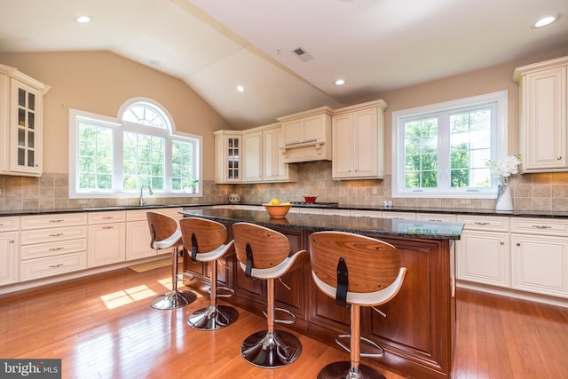 kitchen with visible vents, dark stone counters, lofted ceiling, light wood-style floors, and custom exhaust hood