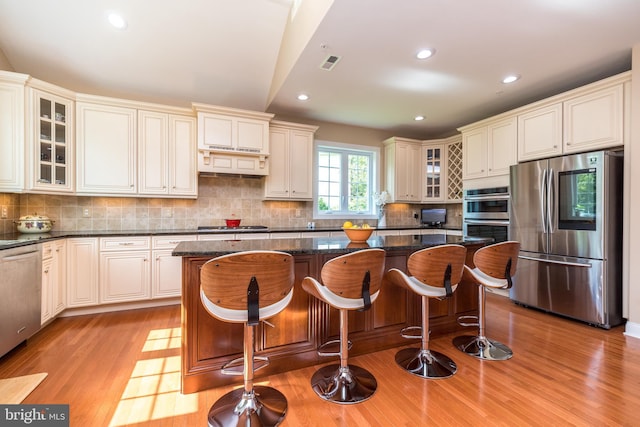 kitchen featuring visible vents, light wood-style flooring, glass insert cabinets, appliances with stainless steel finishes, and a center island