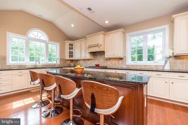 kitchen with a kitchen island, light wood-type flooring, vaulted ceiling, dark stone countertops, and a kitchen breakfast bar