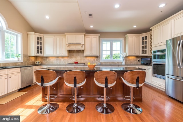 kitchen with tasteful backsplash, light wood-style flooring, appliances with stainless steel finishes, and a kitchen island