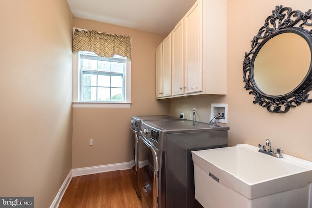 clothes washing area with a sink, washing machine and dryer, wood finished floors, cabinet space, and baseboards