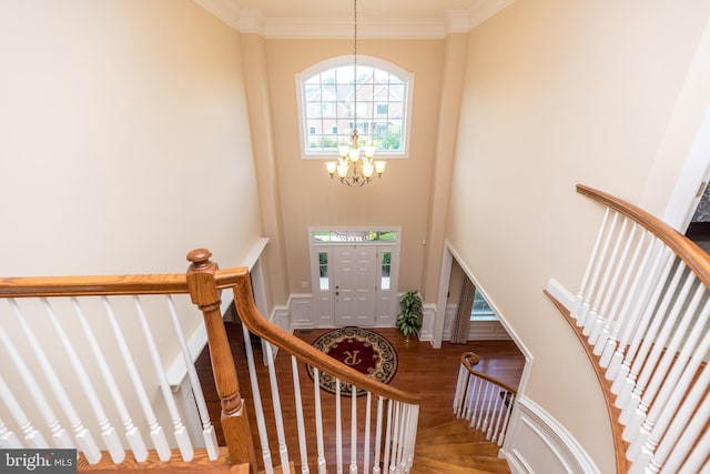 entryway with stairway, wood finished floors, ornamental molding, a towering ceiling, and a notable chandelier