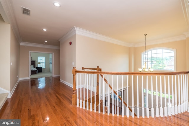 corridor with visible vents, baseboards, ornamental molding, an upstairs landing, and wood finished floors