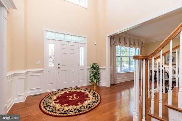 foyer featuring visible vents, wood finished floors, ornamental molding, and a decorative wall