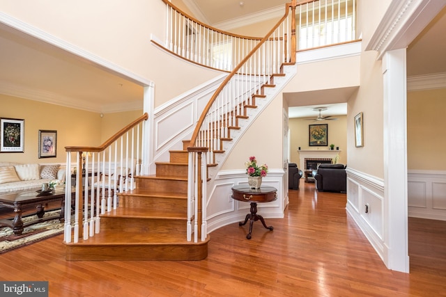 staircase featuring ornamental molding, a ceiling fan, wood finished floors, a fireplace, and a decorative wall