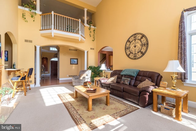 carpeted living room featuring visible vents, arched walkways, a high ceiling, and ornate columns