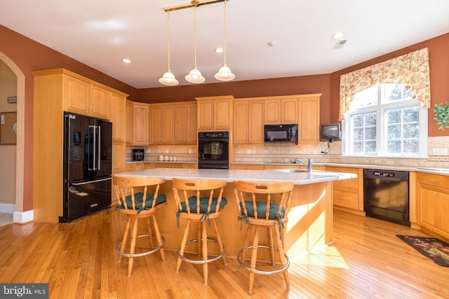 kitchen with light wood-type flooring, black appliances, a center island with sink, arched walkways, and light countertops