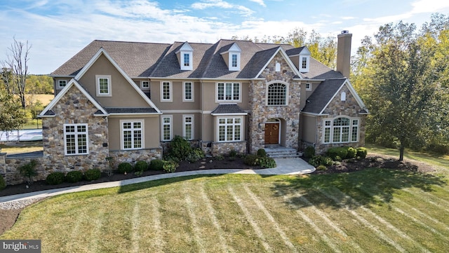 view of front facade with a shingled roof, a front yard, stucco siding, a chimney, and stone siding