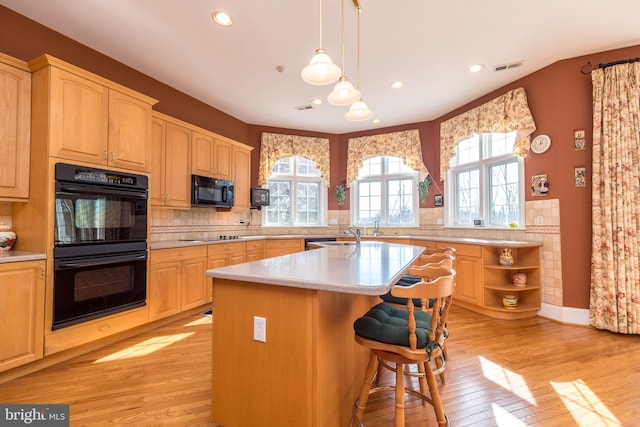 kitchen featuring black appliances, a kitchen breakfast bar, light countertops, and light wood finished floors