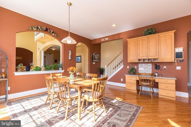 dining area with light wood-style floors, arched walkways, and baseboards