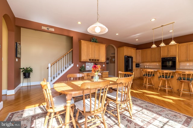 dining area featuring arched walkways, recessed lighting, and light wood-style flooring