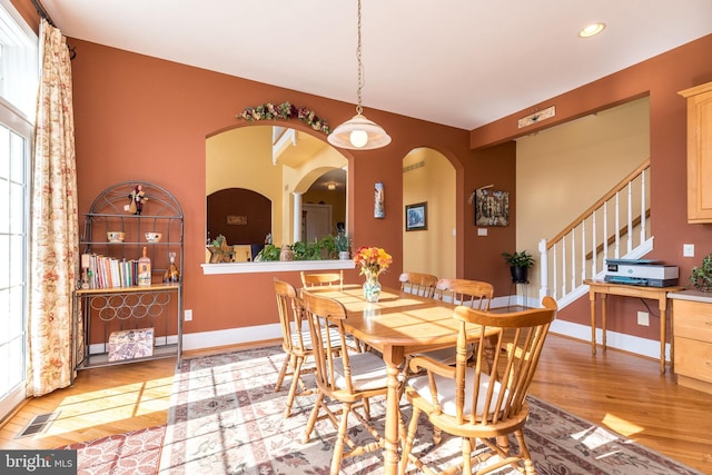 dining area featuring stairway, baseboards, light wood-style flooring, recessed lighting, and arched walkways