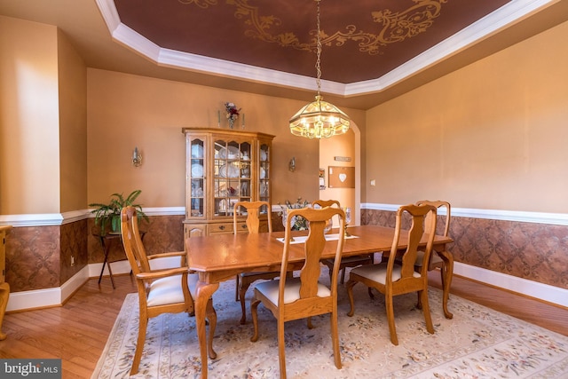 dining area featuring a wainscoted wall, light wood finished floors, wallpapered walls, a raised ceiling, and a chandelier