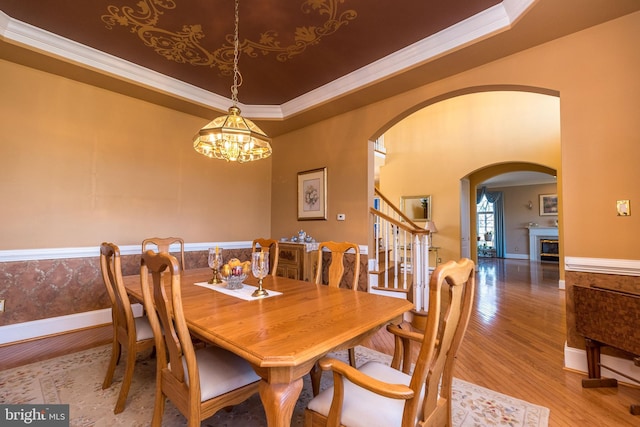 dining space featuring a tray ceiling, arched walkways, wood finished floors, and crown molding