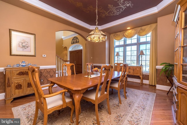 dining area featuring light wood-style flooring, arched walkways, ornamental molding, a raised ceiling, and a notable chandelier