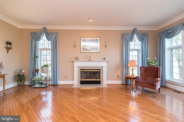 living area featuring baseboards, visible vents, a fireplace with flush hearth, ornamental molding, and light wood-style floors