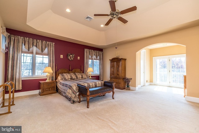 carpeted bedroom with a tray ceiling, arched walkways, multiple windows, and visible vents