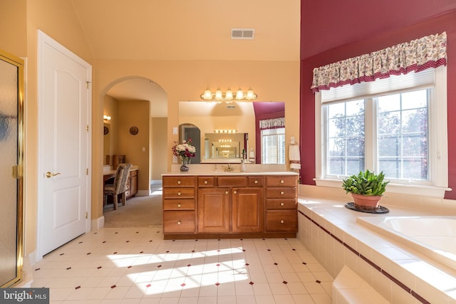 bathroom with vanity, vaulted ceiling, visible vents, and tiled bath