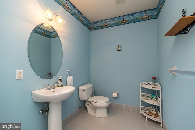 half bathroom featuring tile patterned floors, visible vents, toilet, a sink, and baseboards