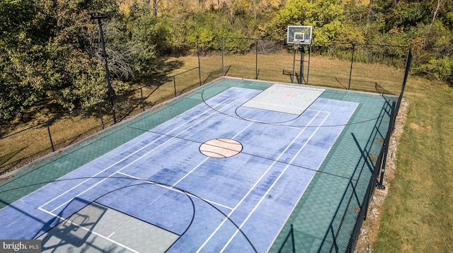 view of basketball court with basketball hoop, a yard, and fence