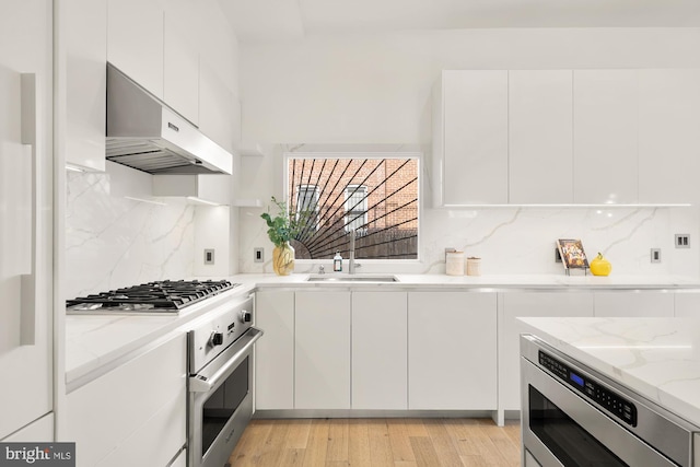 kitchen with under cabinet range hood, a sink, white cabinetry, appliances with stainless steel finishes, and light stone countertops