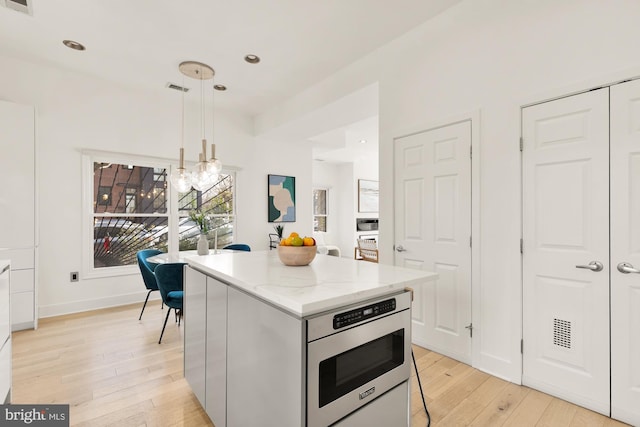 kitchen featuring a center island, visible vents, light wood-style floors, hanging light fixtures, and light stone countertops