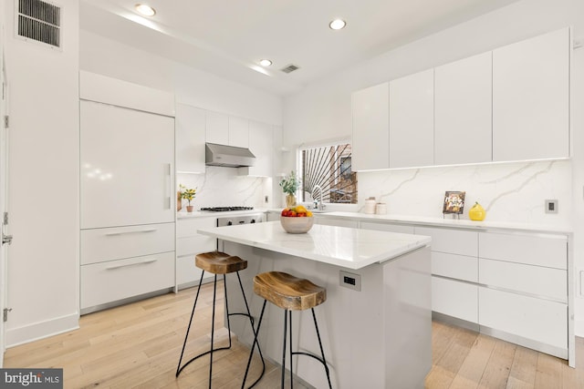 kitchen with visible vents, light wood-style flooring, modern cabinets, under cabinet range hood, and white cabinetry