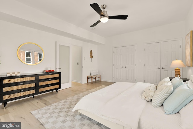 bedroom with ceiling fan, light wood finished floors, two closets, and baseboards