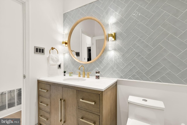 half bathroom with tasteful backsplash, visible vents, vanity, and toilet