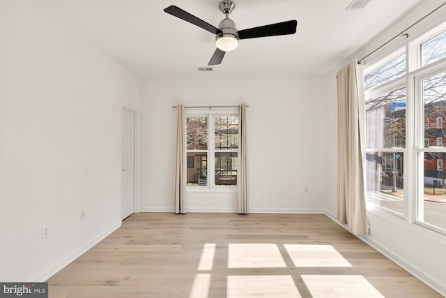 spare room with light wood finished floors, a wealth of natural light, visible vents, and baseboards