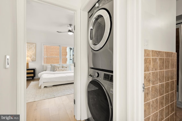 clothes washing area with laundry area, wood finished floors, a ceiling fan, tile walls, and stacked washer and clothes dryer