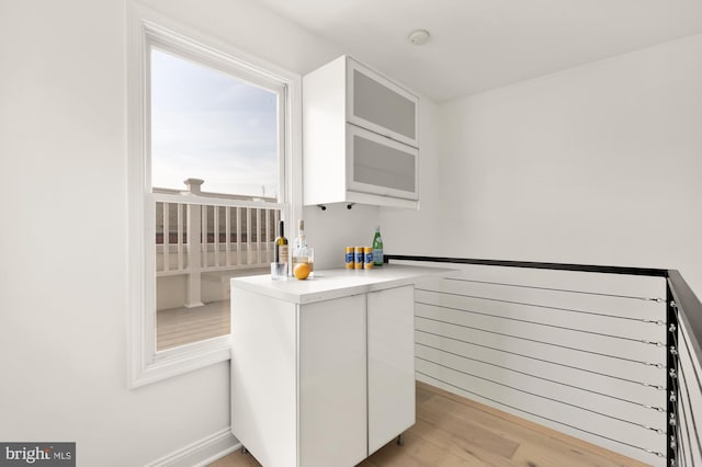 interior space featuring light wood-style floors, light countertops, white cabinets, and glass insert cabinets