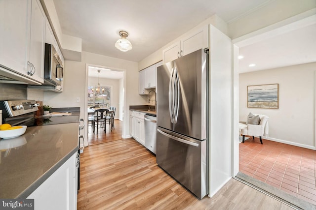 kitchen featuring baseboards, light wood-style floors, white cabinets, appliances with stainless steel finishes, and dark countertops