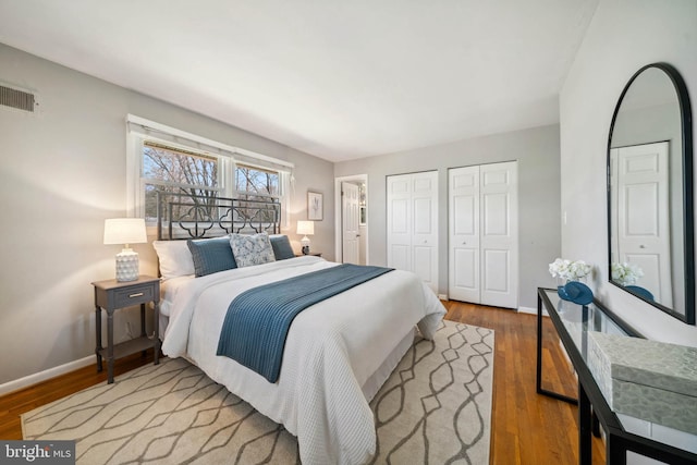 bedroom with wood finished floors, visible vents, baseboards, and two closets