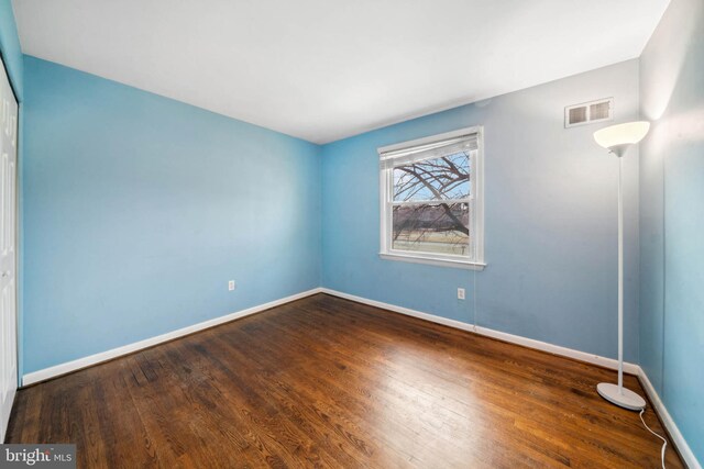 unfurnished bedroom with a closet, wood finished floors, visible vents, and baseboards