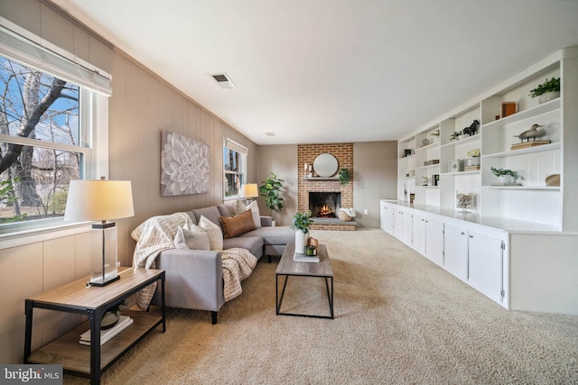 carpeted living area featuring a brick fireplace, plenty of natural light, and visible vents