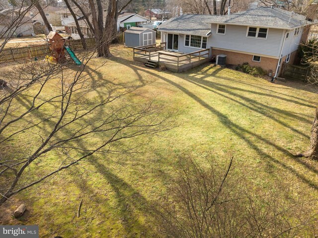 view of yard with an outbuilding, fence, a wooden deck, a shed, and central AC