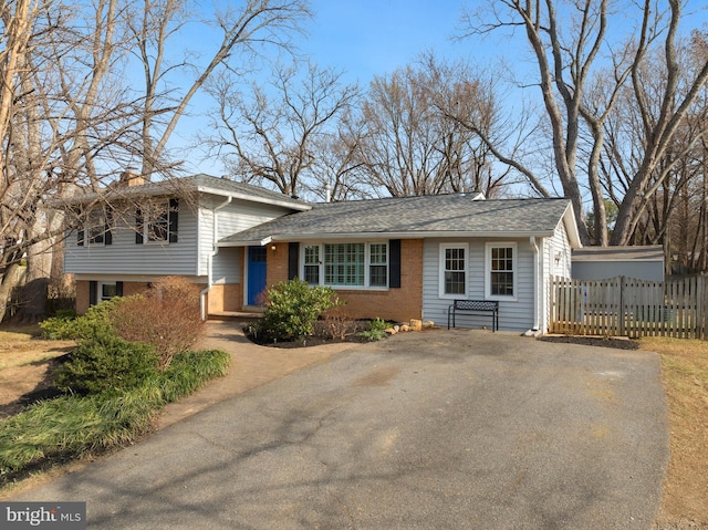 split level home featuring a shingled roof, brick siding, fence, and driveway