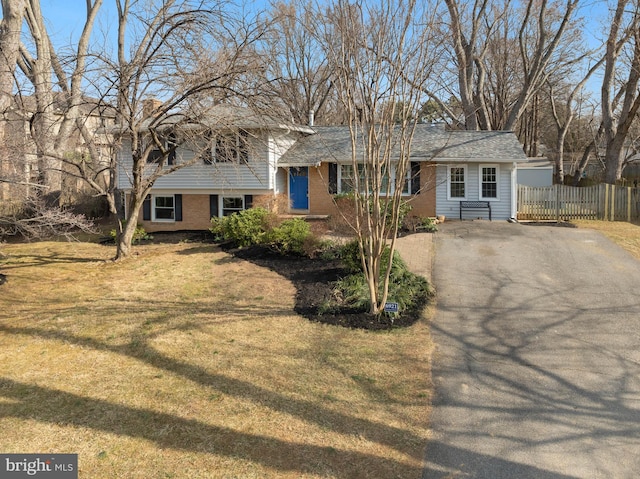 tri-level home featuring driveway, fence, a front lawn, and brick siding