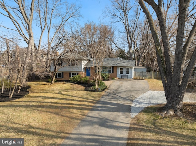 tri-level home with driveway, brick siding, a front lawn, and fence