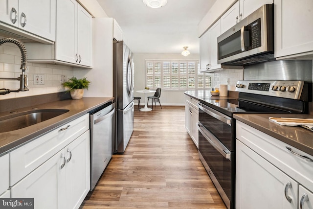 kitchen with stainless steel appliances, a sink, white cabinetry, light wood-type flooring, and backsplash