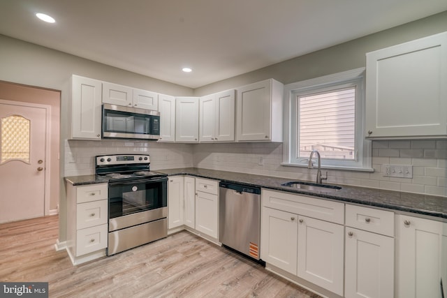 kitchen with light wood-style floors, dark stone countertops, appliances with stainless steel finishes, and a sink