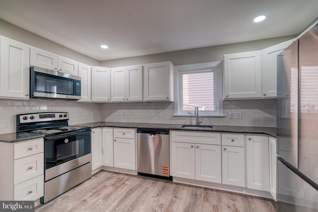 kitchen featuring a sink, white cabinets, appliances with stainless steel finishes, light wood-type flooring, and dark stone countertops