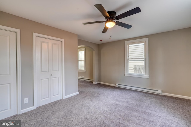 unfurnished bedroom with a baseboard heating unit, arched walkways, carpet floors, and baseboards