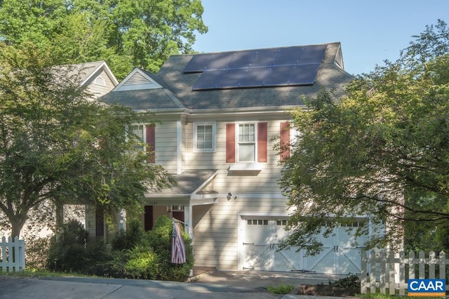 view of front facade with an attached garage, roof mounted solar panels, fence, and roof with shingles