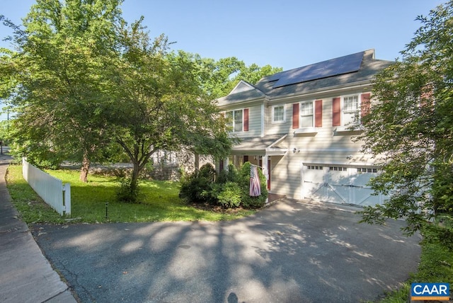 view of front of home with solar panels, aphalt driveway, an attached garage, fence, and a front lawn