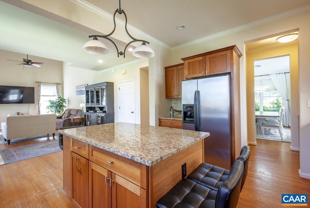 kitchen with light wood-style flooring, brown cabinetry, a kitchen island, light stone countertops, and stainless steel fridge with ice dispenser